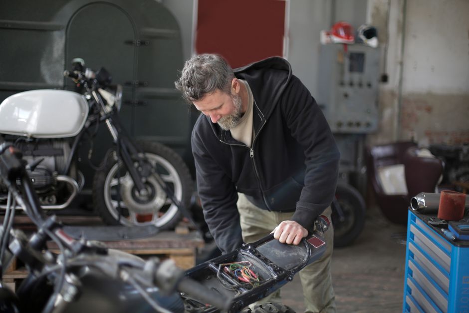 Middle aged bearded male mechanic in workwear repairing electric parts of motorbike while working in modern garage
